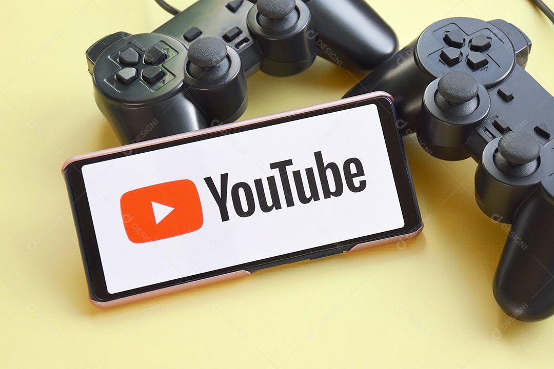 Smartphone com tela do YouTube e dois controle de jogo em fundo amarelo