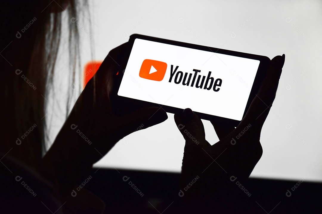 Jovem com celular nas mãos com tela de youtube contra fundo de monitor