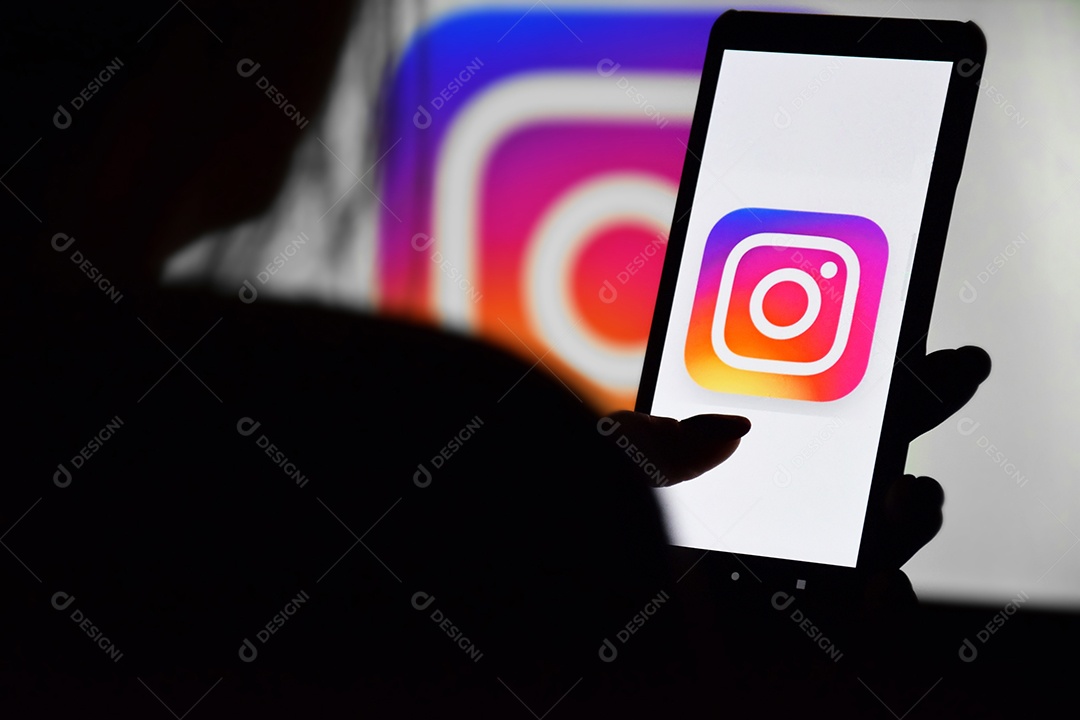Rede social mostrada em celular nas mãos de uma mulher e fundo de monitor