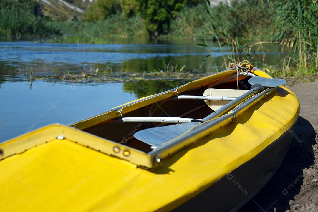 Caiaque amarelo na margem de um rio com fundo de matas verdes