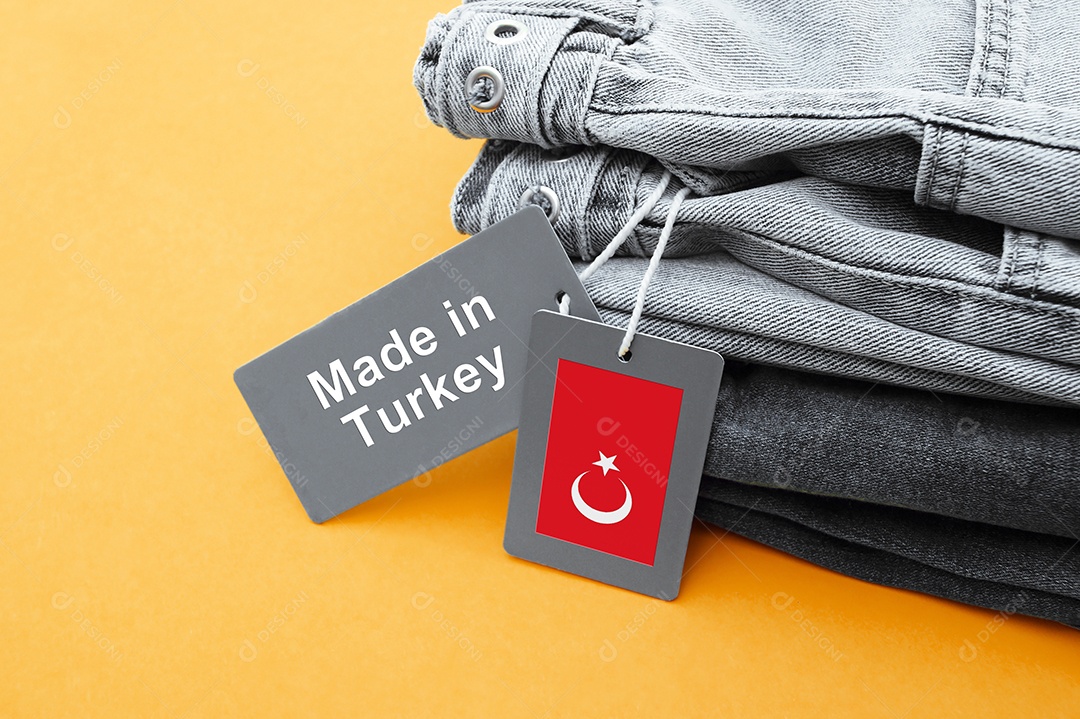 Detalhe de jeans preto etiquetas cinza e inscrição fabricado na Turquia em fundo amarelo