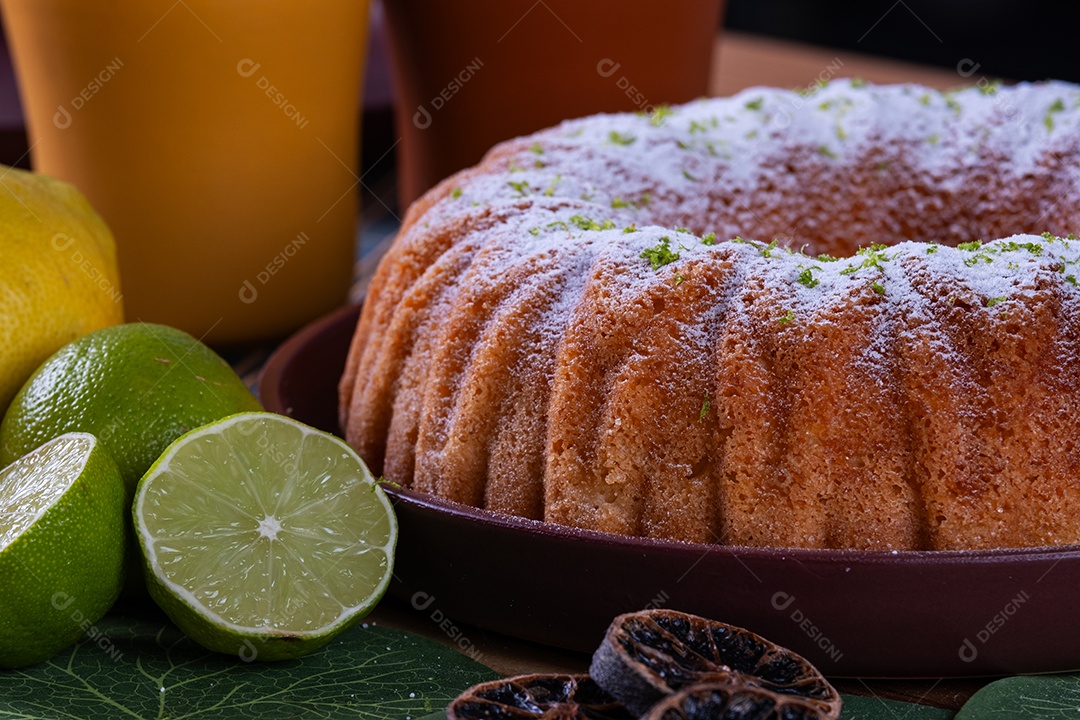 Delicioso bolo de limão na mesa com copos e limões ao lado.