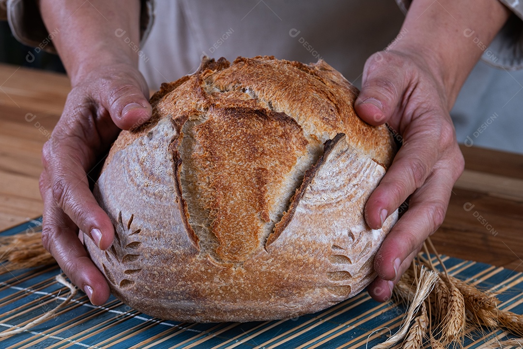 Mãos femininas segurando pão artesanal de fermentação natural.