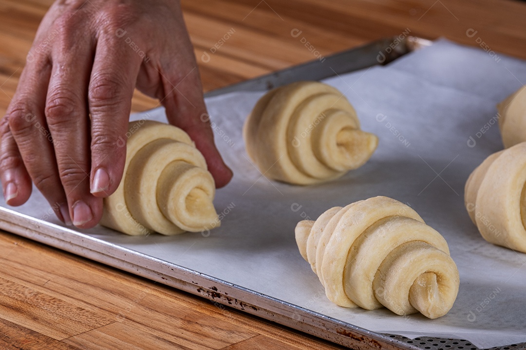 Mão de uma mulher colocando um croissant em uma assadeira para ir ao forno.