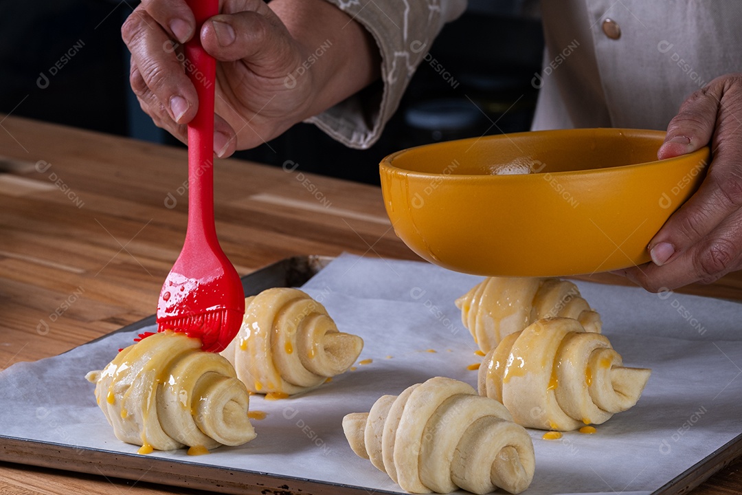 Mão de uma mulher colocando um croissant em uma assadeira para ir ao forno.