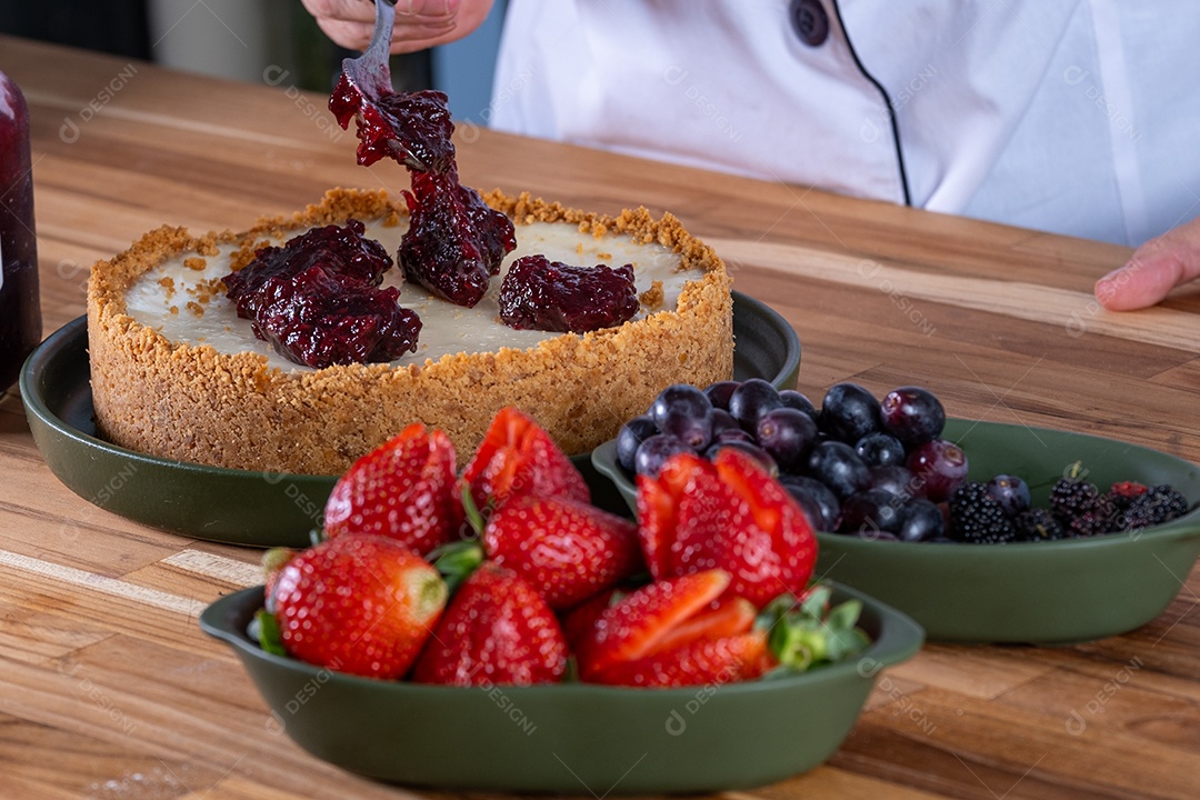 Mão com colher espalhando geléia de frutas vermelhas na torta doce