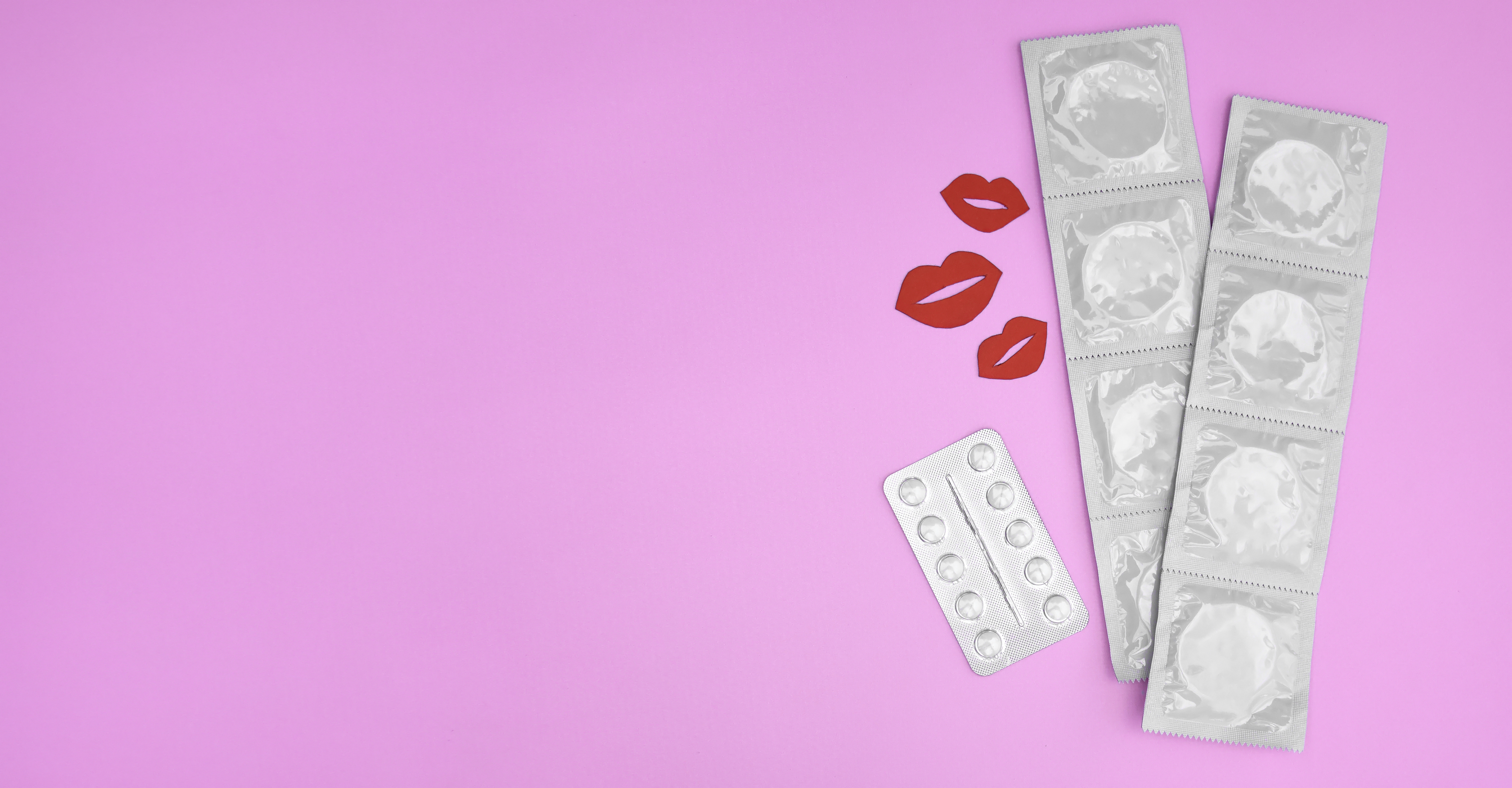 Muitos pacotes brancos de preservativos fechados em um fundo rosa