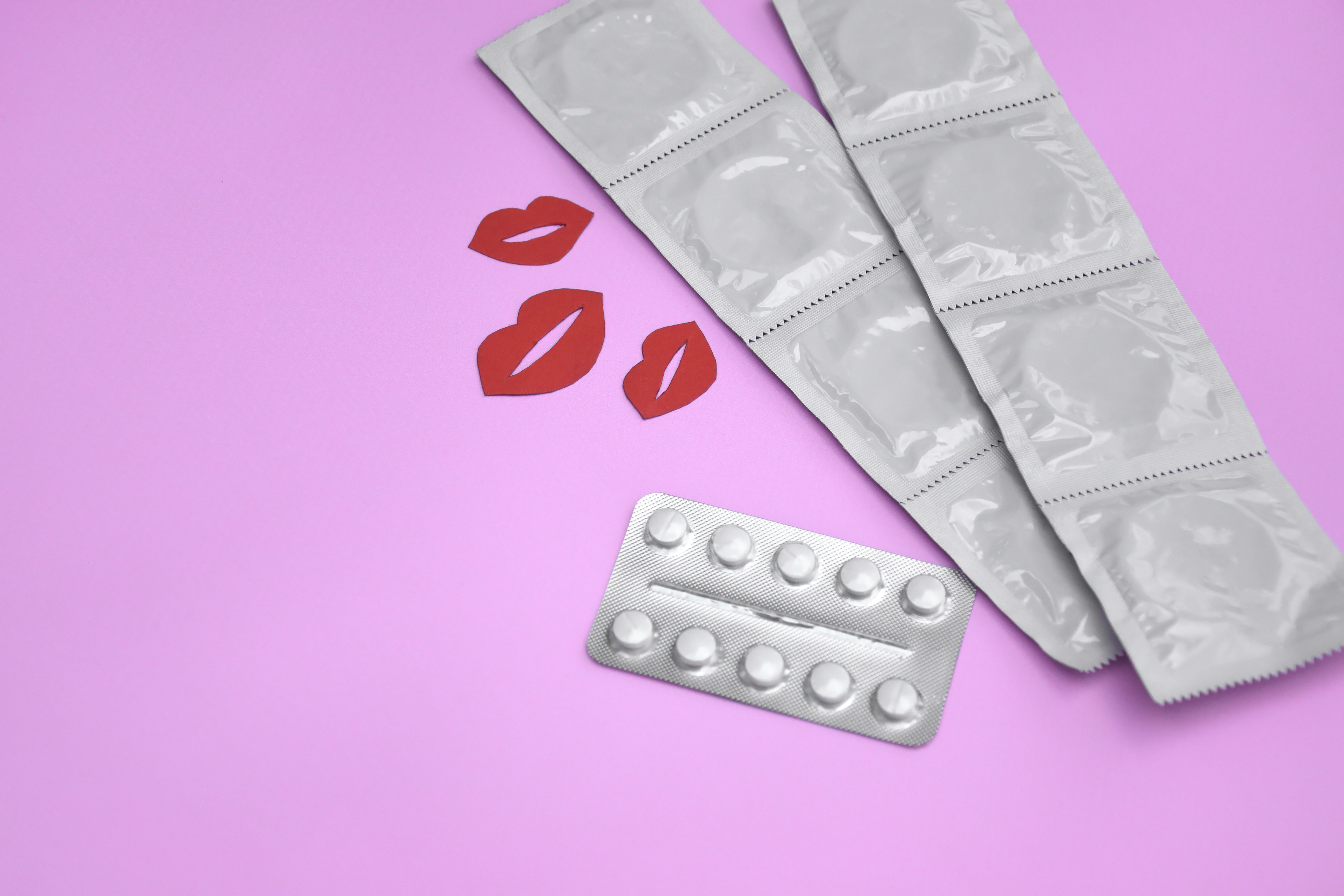 Muitos pacotes brancos de preservativos fechados em um fundo rosa
