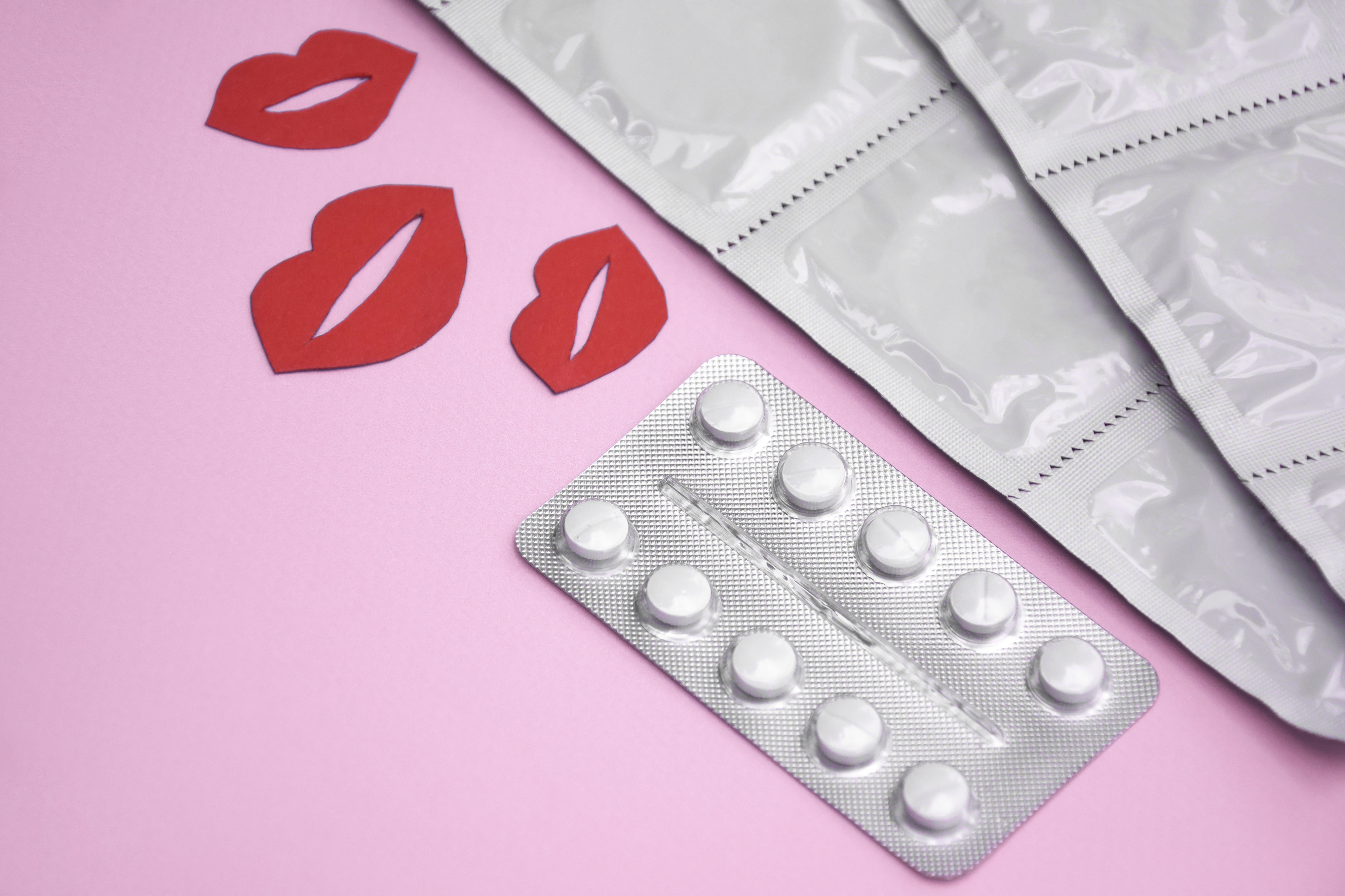 Preservativo e comprimido sobre fundo colorido rosa