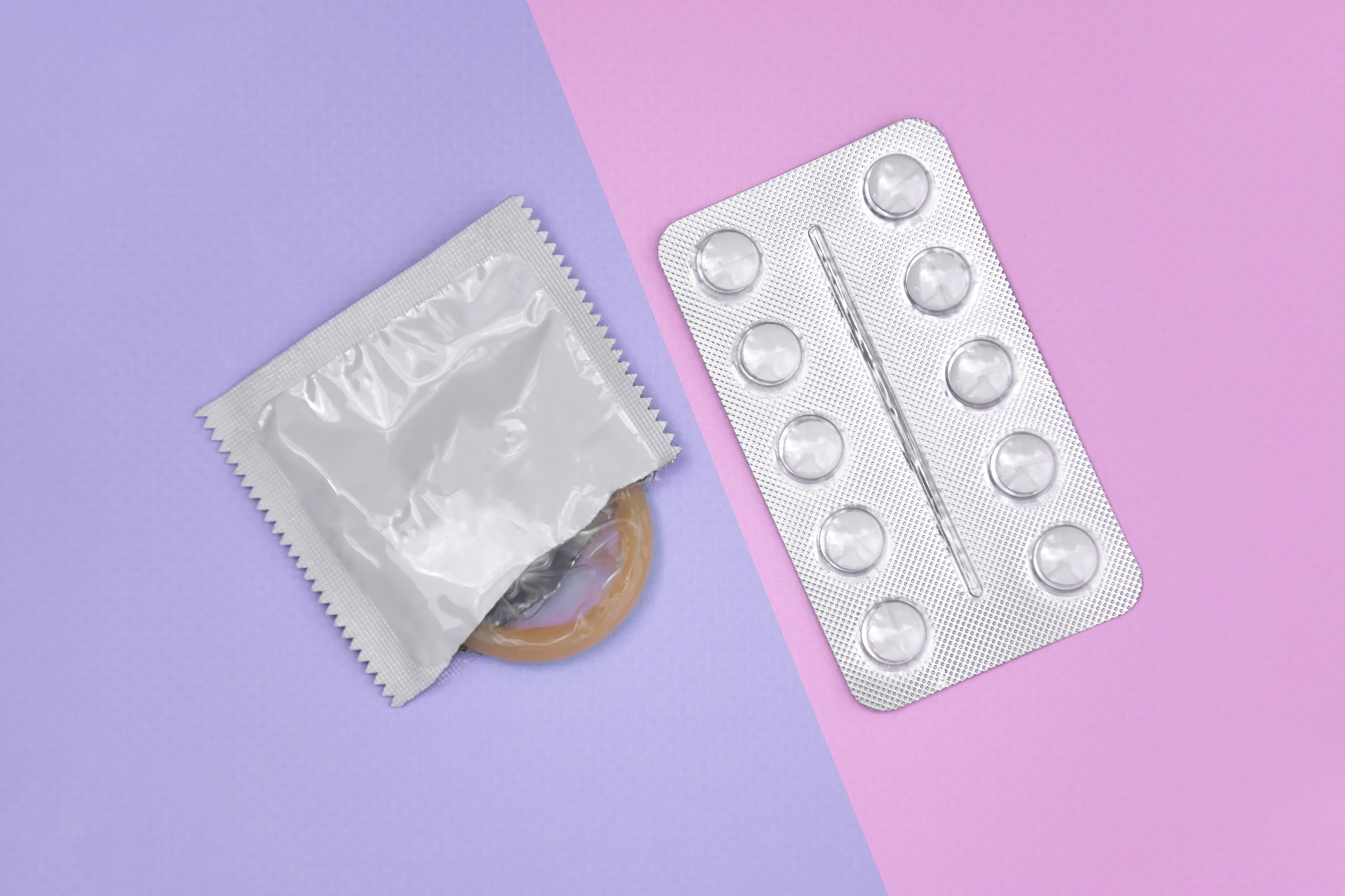 Preservativo e comprimido sobre fundo colorido rosa e lilás