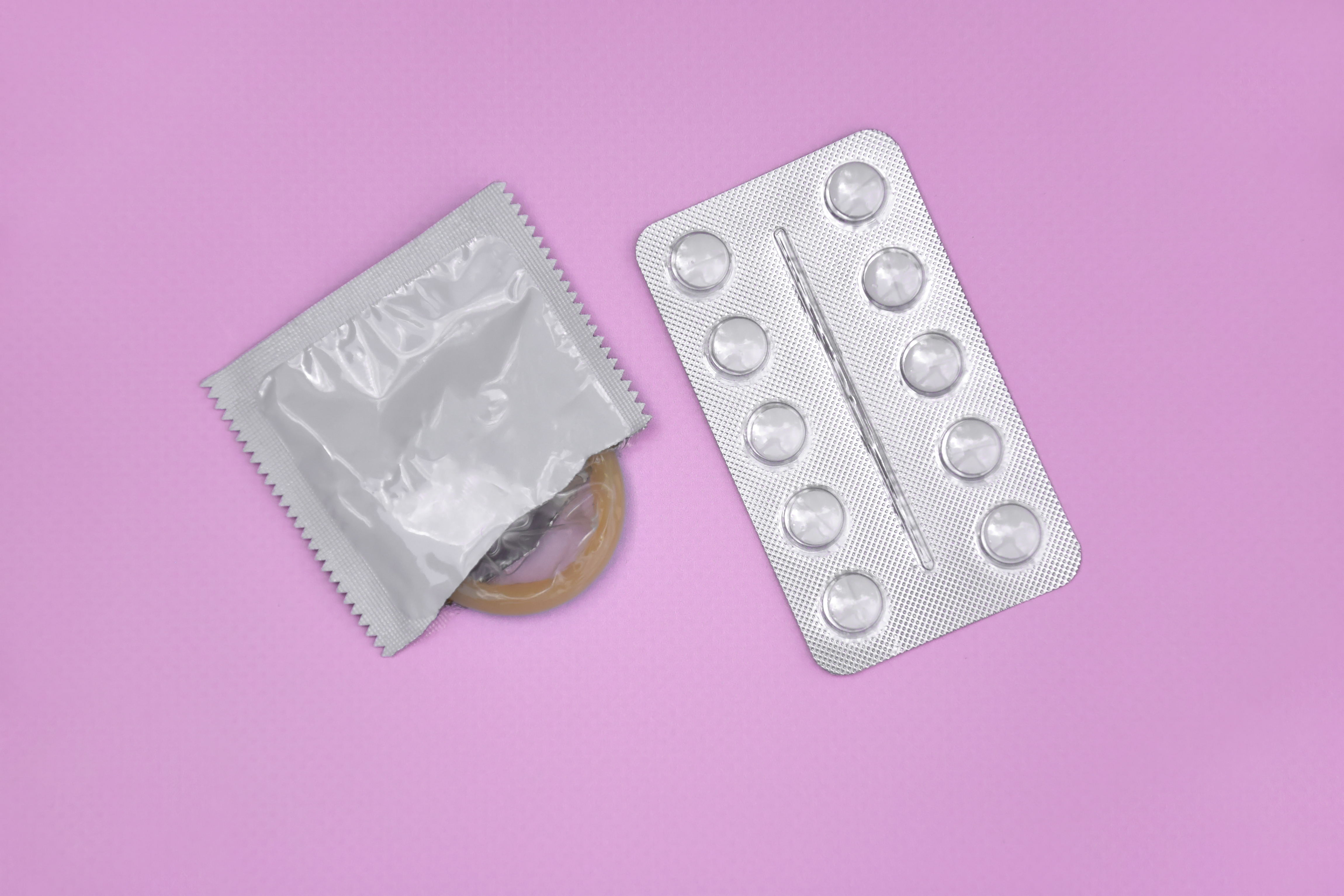 Comprimidos e preservativo sobre fundo lilás