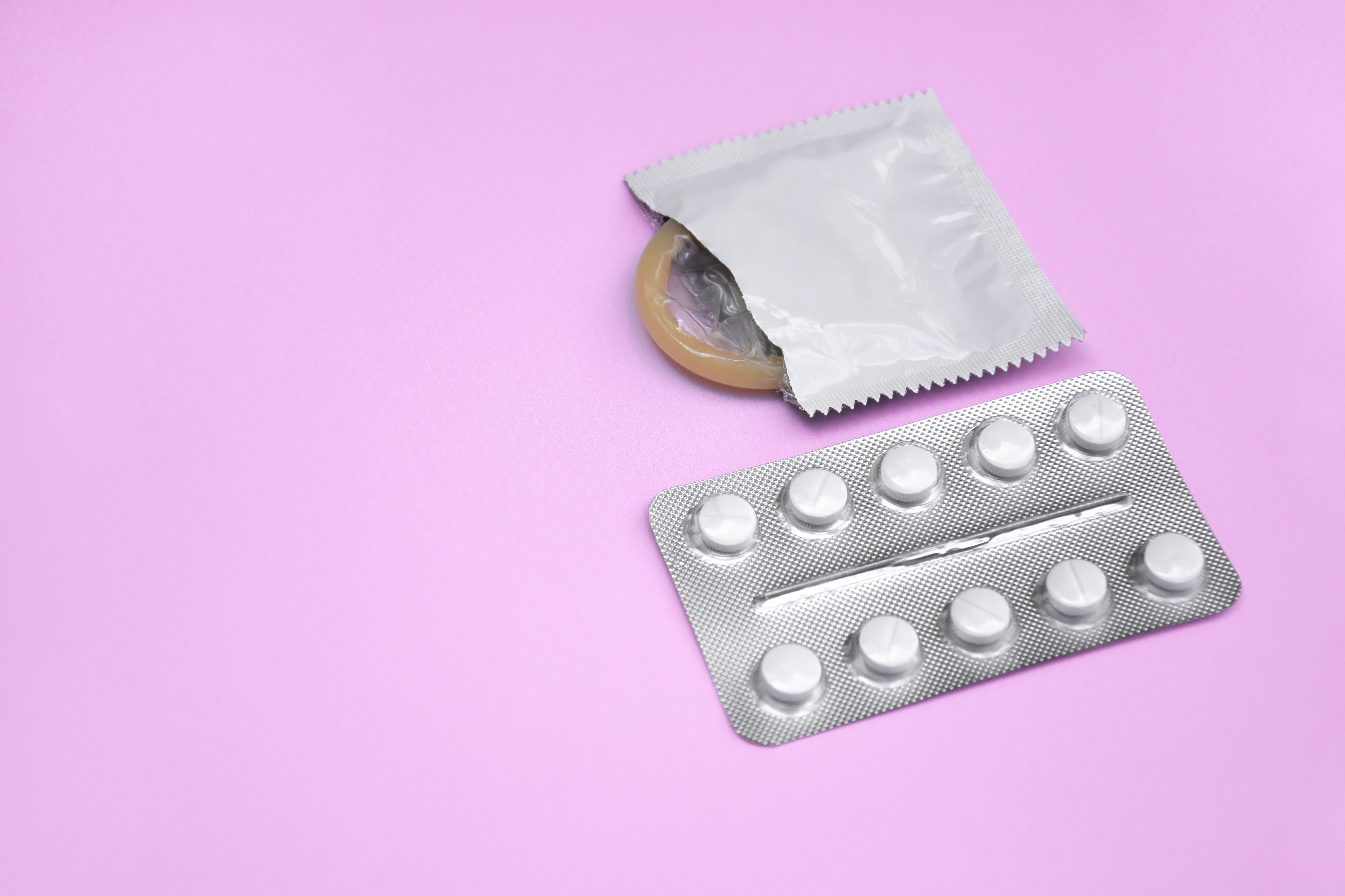 Comprimido e preservativo sobre fundo lilás