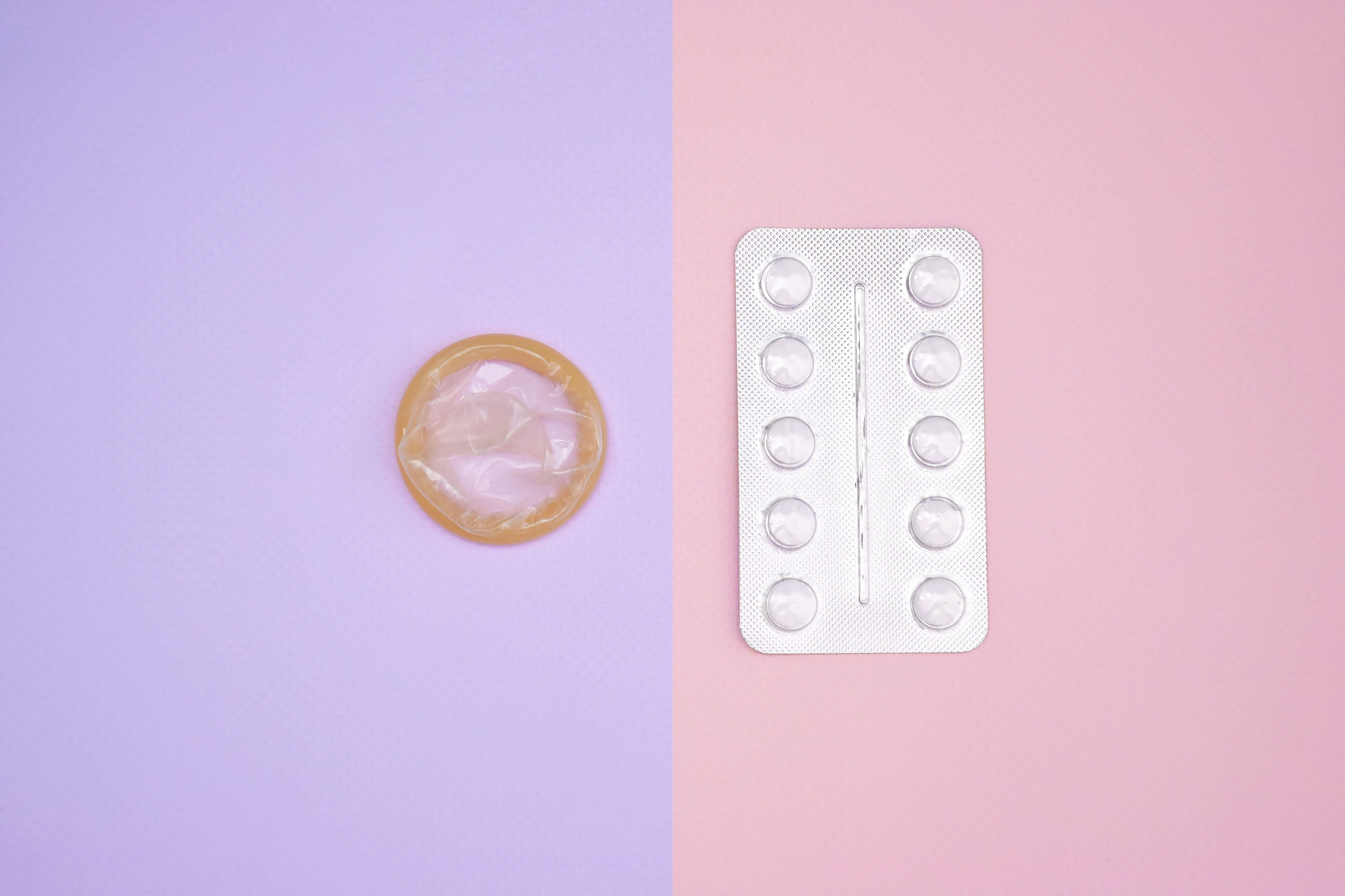 Preservativo e comprimido sobre fundo colorido rosa e lilás