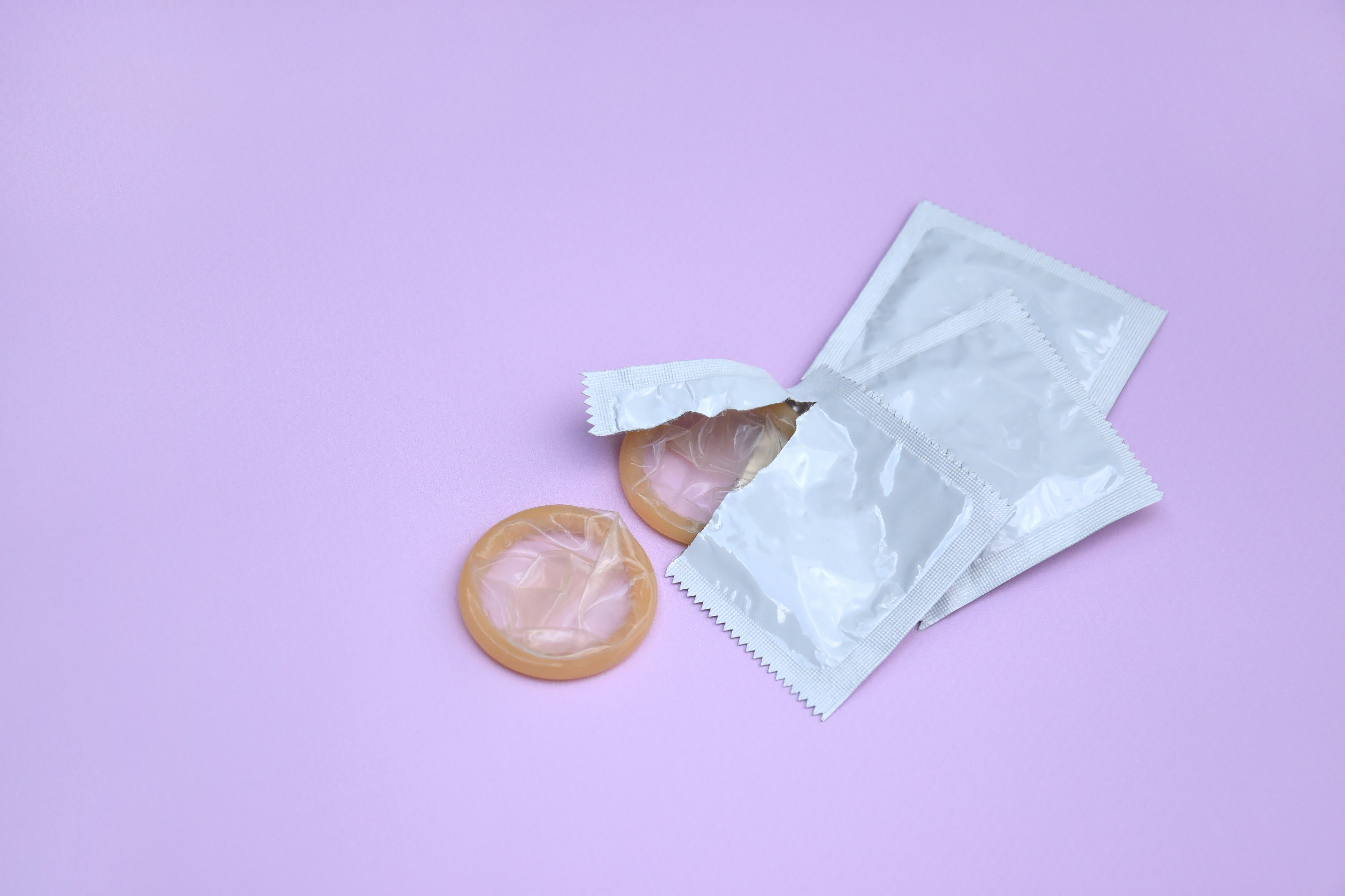 Preservativo de embalagem branca sobre fundo lilás