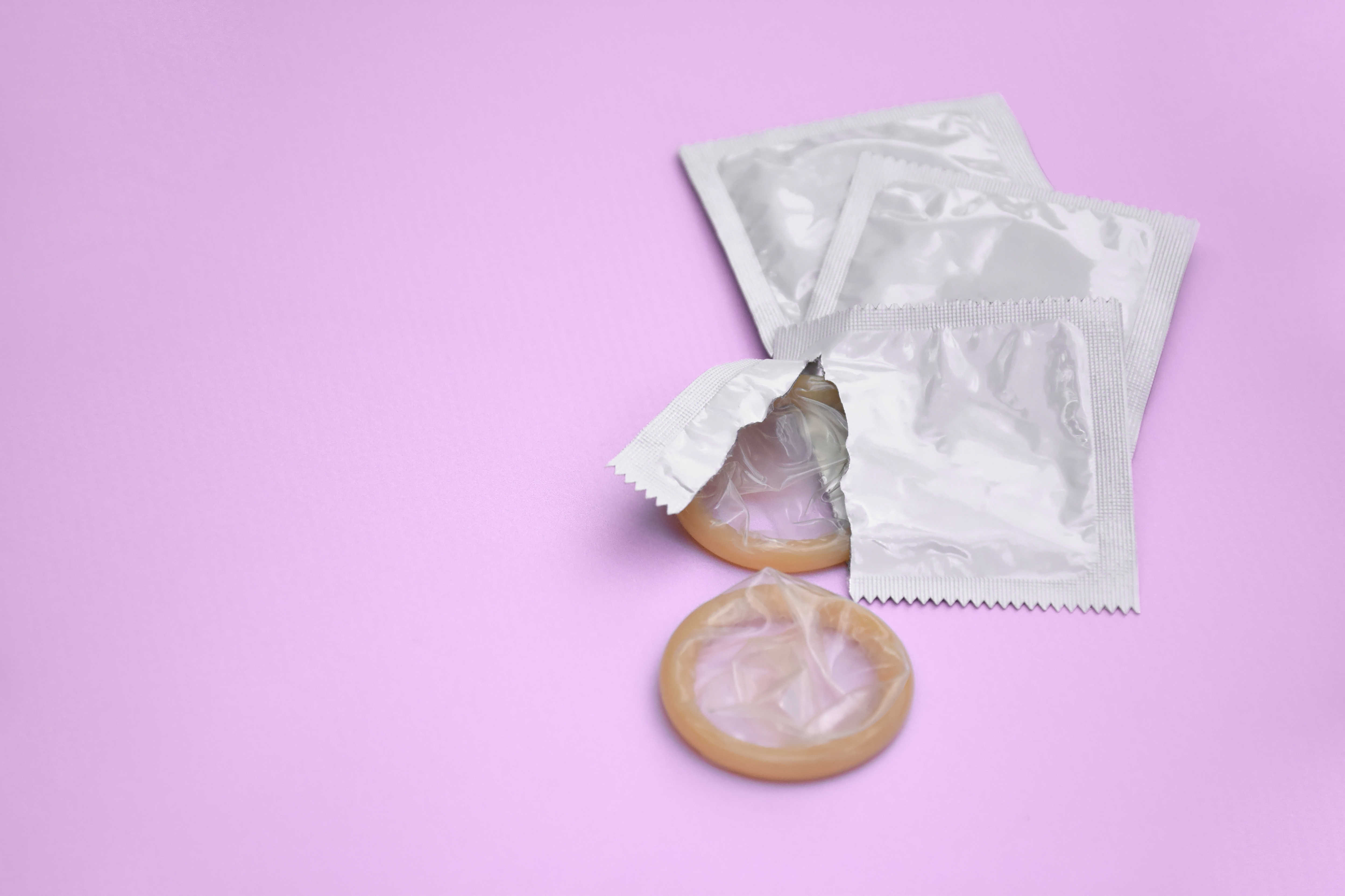 Preservativo de embalagem branca sobre fundo lilás