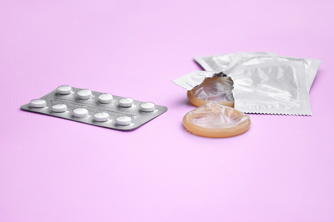 Comprimidos e preservativo sobre fundo lilás