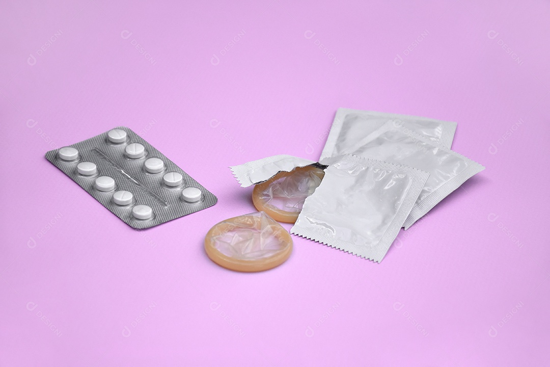 Comprimidos e preservativo sobre fundo lilás