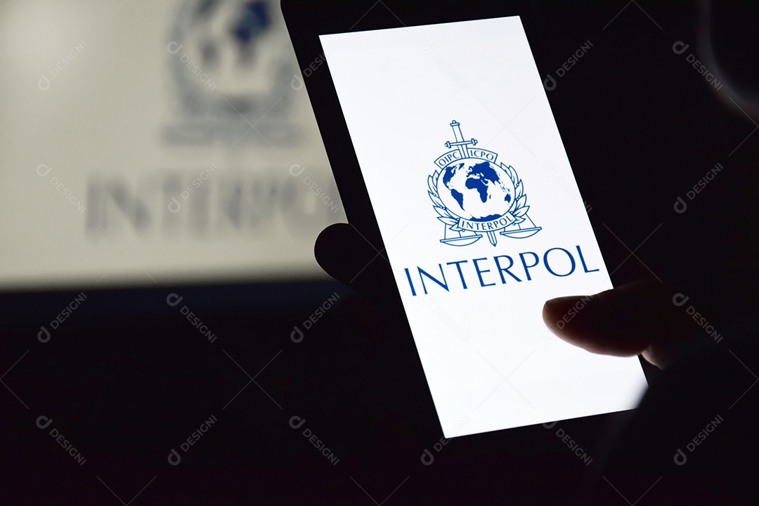 Pessoa segurando celular com logotipo da Interpol exibido na tela