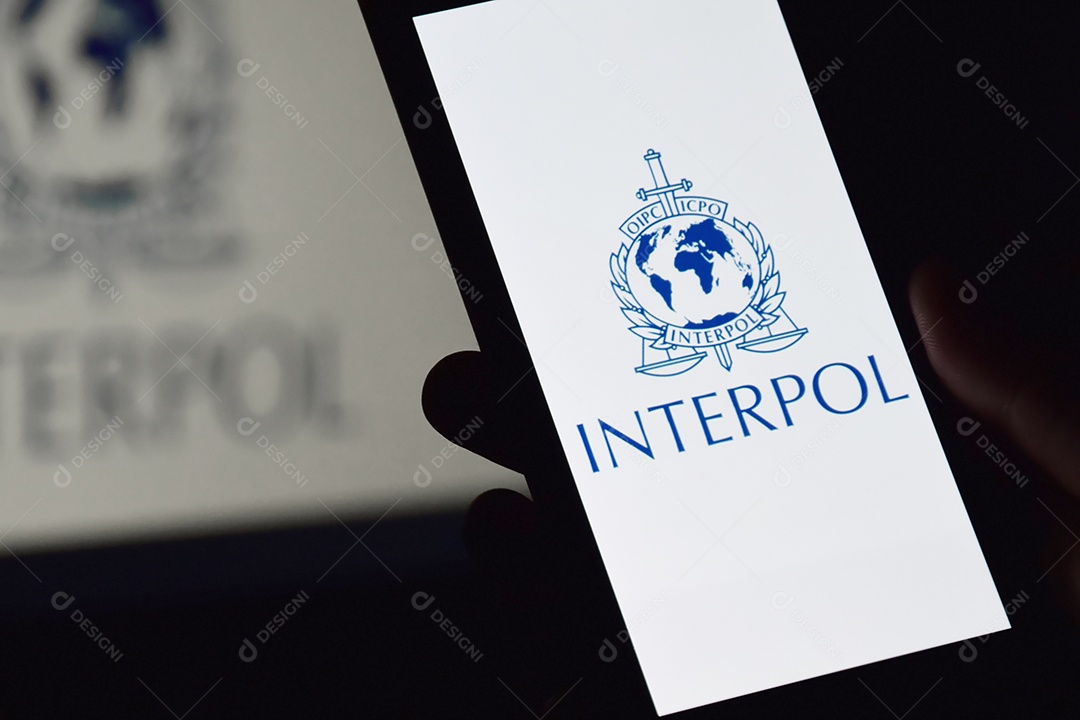 Pessoa segurando celular com logotipo da Interpol exibido na tela