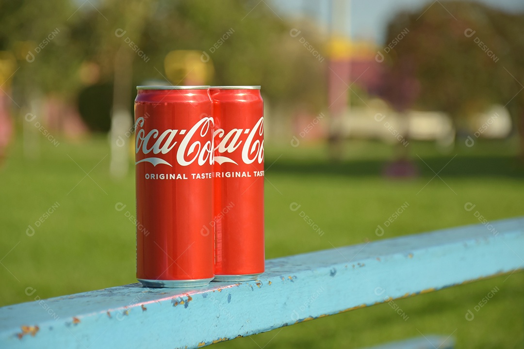 Duas latas de Coca-cola em cima de tábua azul sobre fundo gramado
