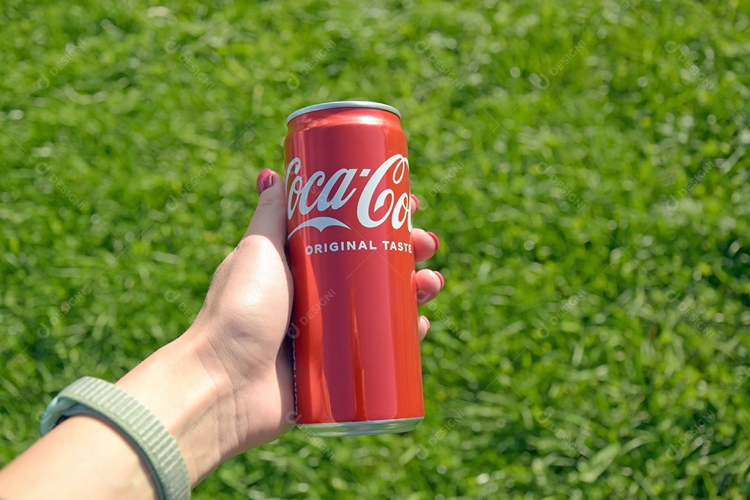 Mão segurando lata de Coca-cola em fundo gramado