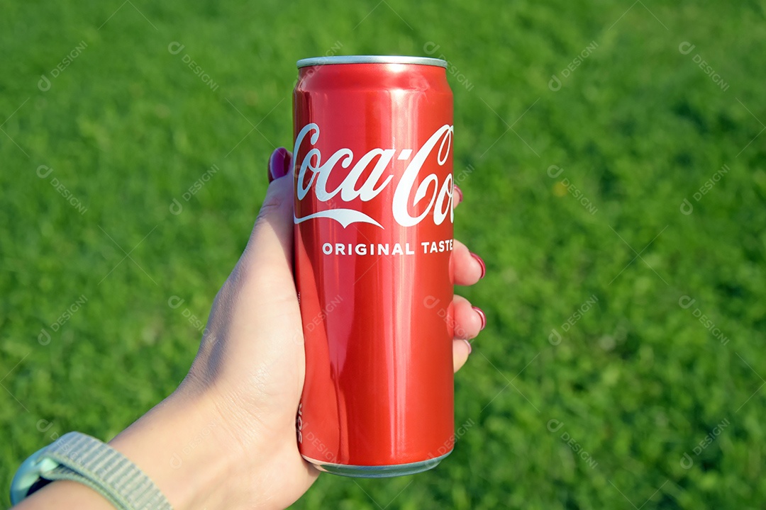 Mão feminina segurando lata de Coca-cola sobre fundo gramado