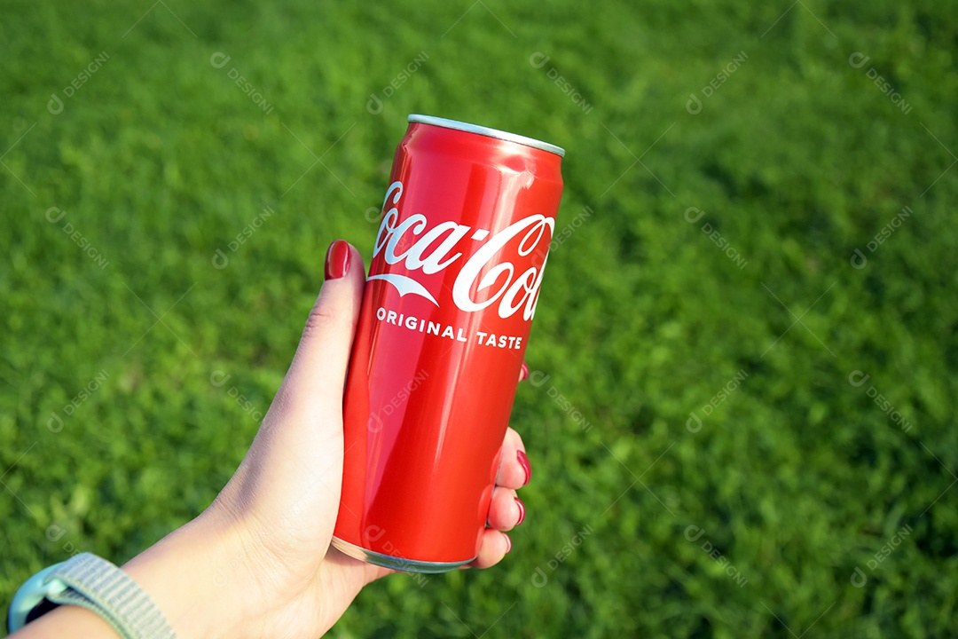 Mão feminina segurando lata de Coca-cola sobre fundo gramado