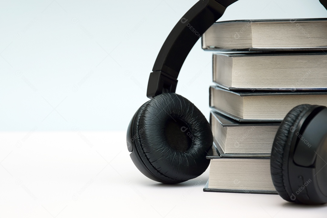 Fones de ouvido pretos com pilha de livros sobre fundo claro