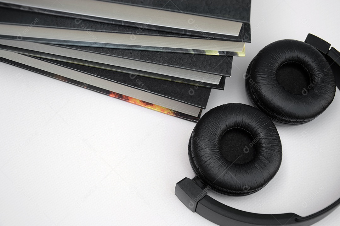 Fones de ouvido pretos com pilha de livros sobre fundo claro