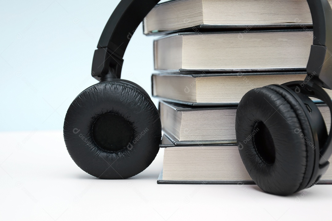 Fones de ouvido pretos com pilha de livros sobre fundo claro