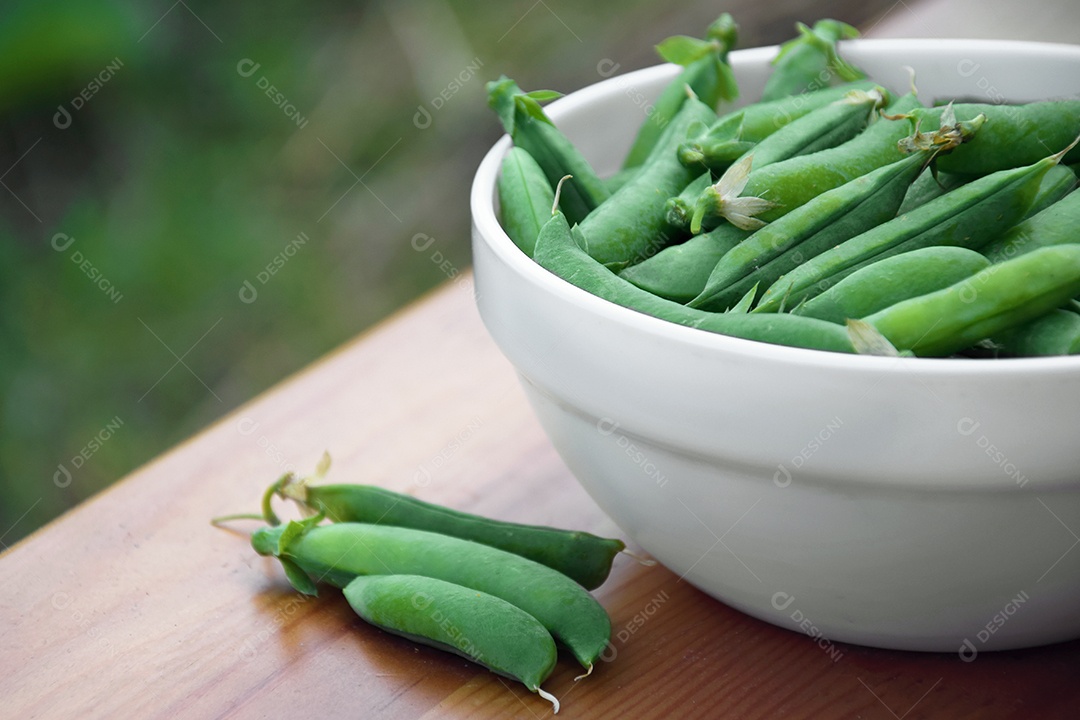 Ervilhas verdes em um prato branco sobre um banco de madeira. Temporada de colheita. Colheita orgânica.