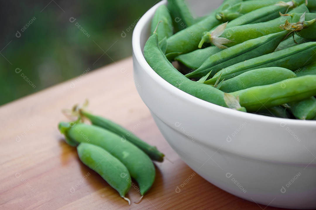 Ervilhas verdes em um prato branco sobre um banco de madeira. Temporada de colheita. Colheita orgânica.