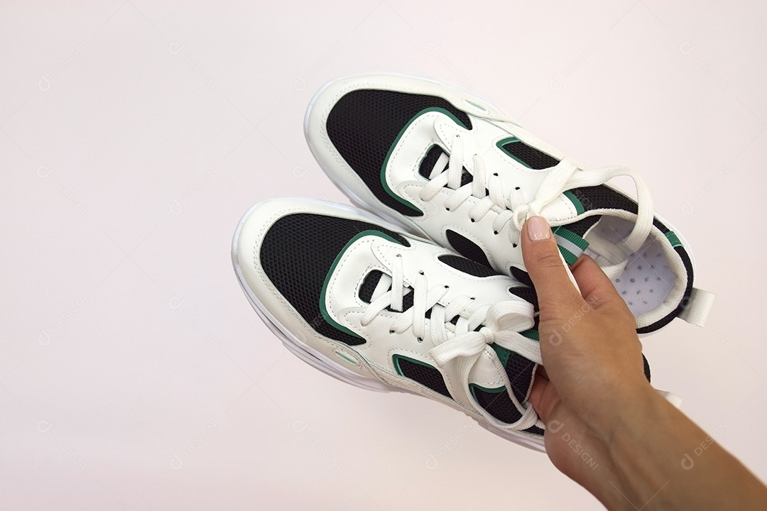 Mão segurando tênis lindo sobre fundo rosa claro