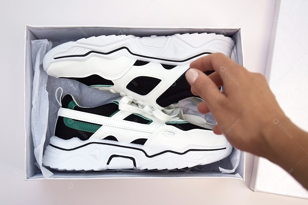 Tênis femininos dentro de uma caixa em fundo claro com mão masculina
