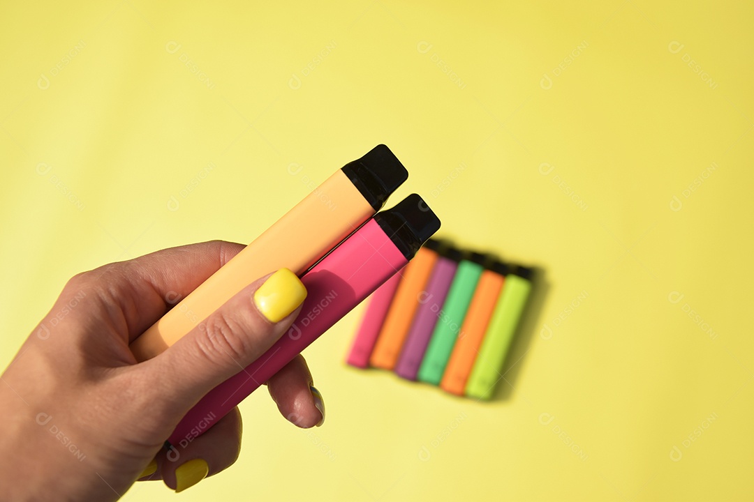 Mão feminina segurando cigarro eletrônico sobre fundo amarelo
