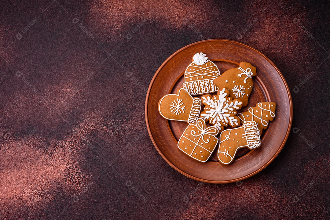 Lindos biscoitos de gengibre de Natal de cores diferentes em uma placa de cerâmica sobre uma mesa de concreto escuro