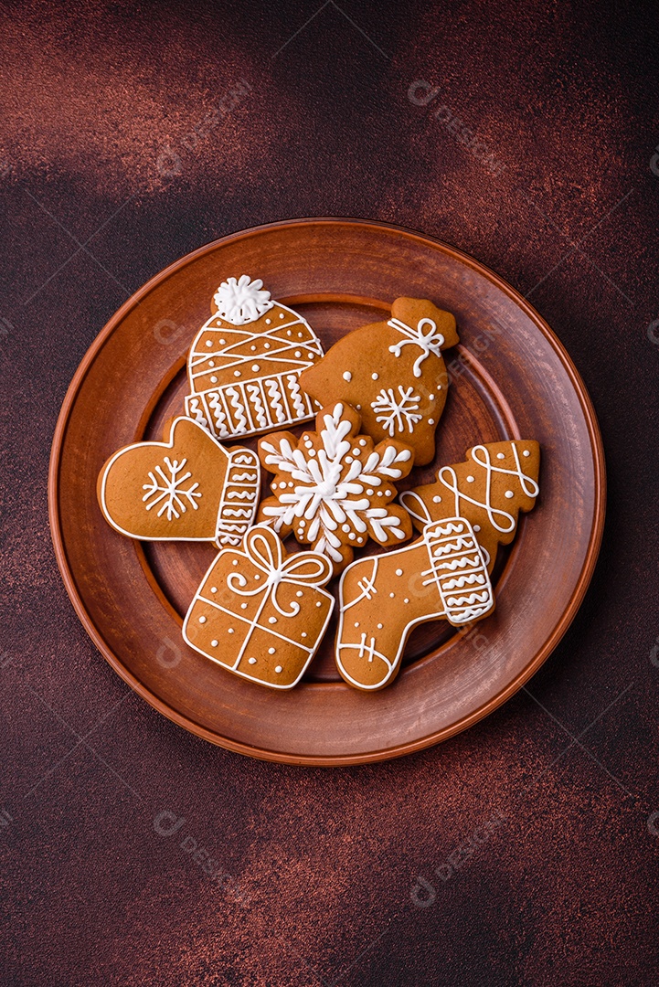 Lindos biscoitos de gengibre de Natal de cores diferentes em uma placa de cerâmica sobre uma mesa de concreto escuro