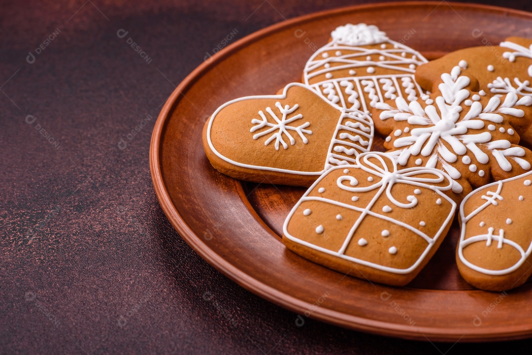Lindos biscoitos de gengibre de Natal de cores diferentes em uma placa de cerâmica sobre uma mesa de concreto escuro