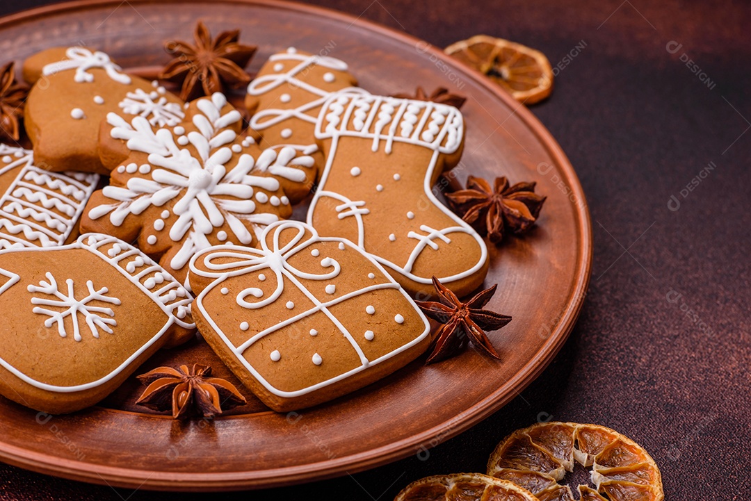 Lindos biscoitos de gengibre de Natal de cores diferentes em uma placa de cerâmica sobre uma mesa de concreto escuro