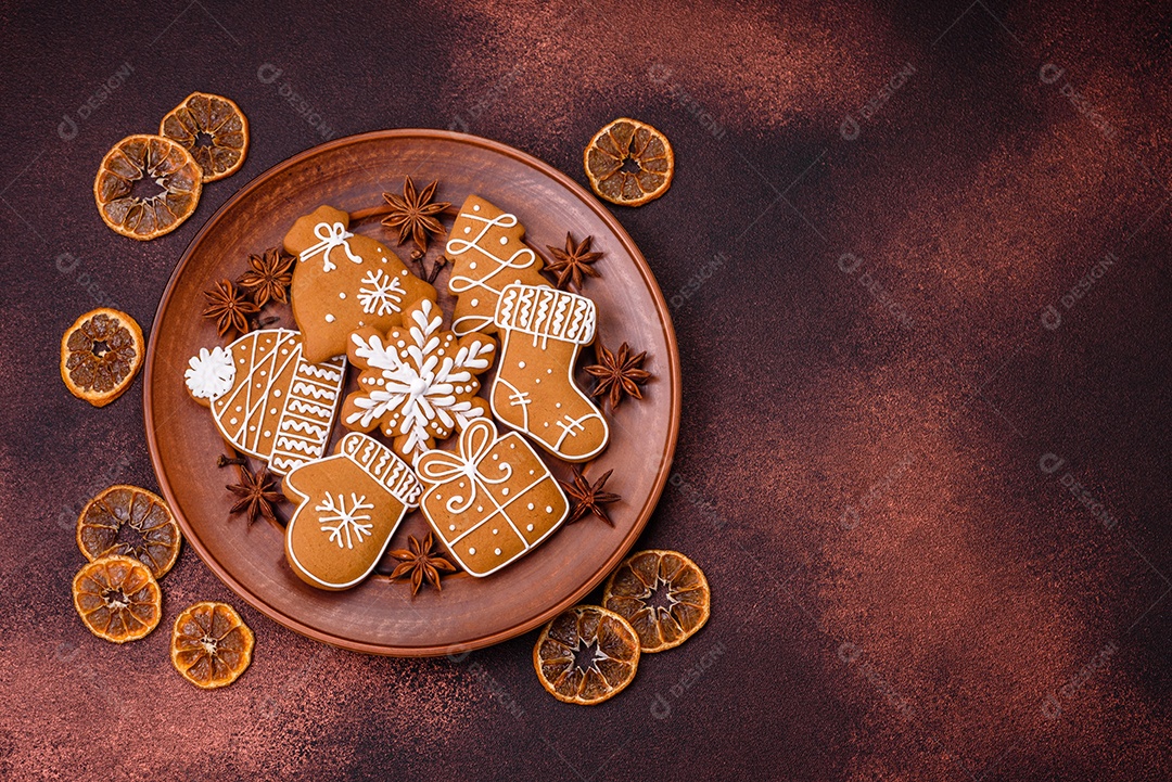 Lindos biscoitos de gengibre de Natal de cores diferentes em uma placa de cerâmica sobre uma mesa de concreto escuro