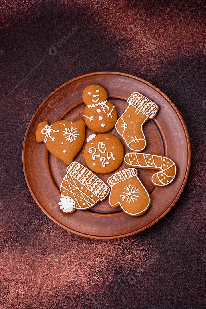 Lindos biscoitos de gengibre de Natal de cores diferentes em uma placa de cerâmica sobre uma mesa de concreto escuro
