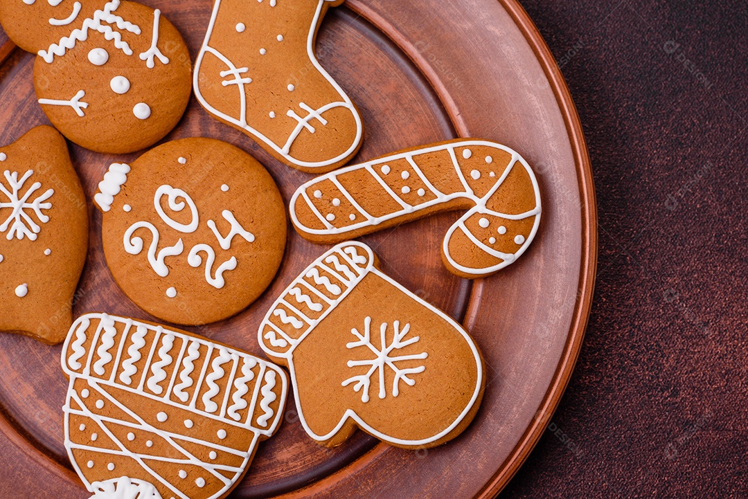 Lindos biscoitos de gengibre de Natal de cores diferentes em uma placa de cerâmica sobre uma mesa de concreto escuro