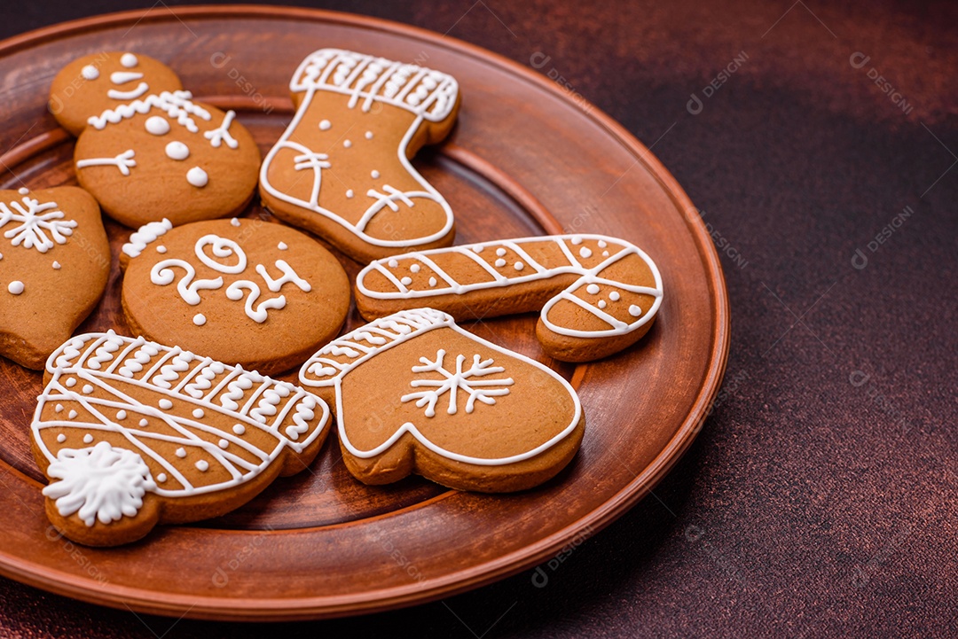 Lindos biscoitos de gengibre de Natal de cores diferentes em uma placa de cerâmica sobre uma mesa de concreto escuro