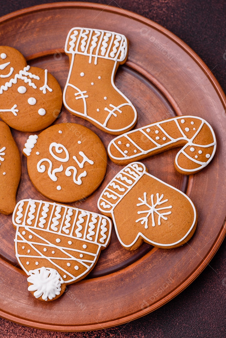 Lindos biscoitos de gengibre de Natal de cores diferentes em uma placa de cerâmica sobre uma mesa de concreto escuro