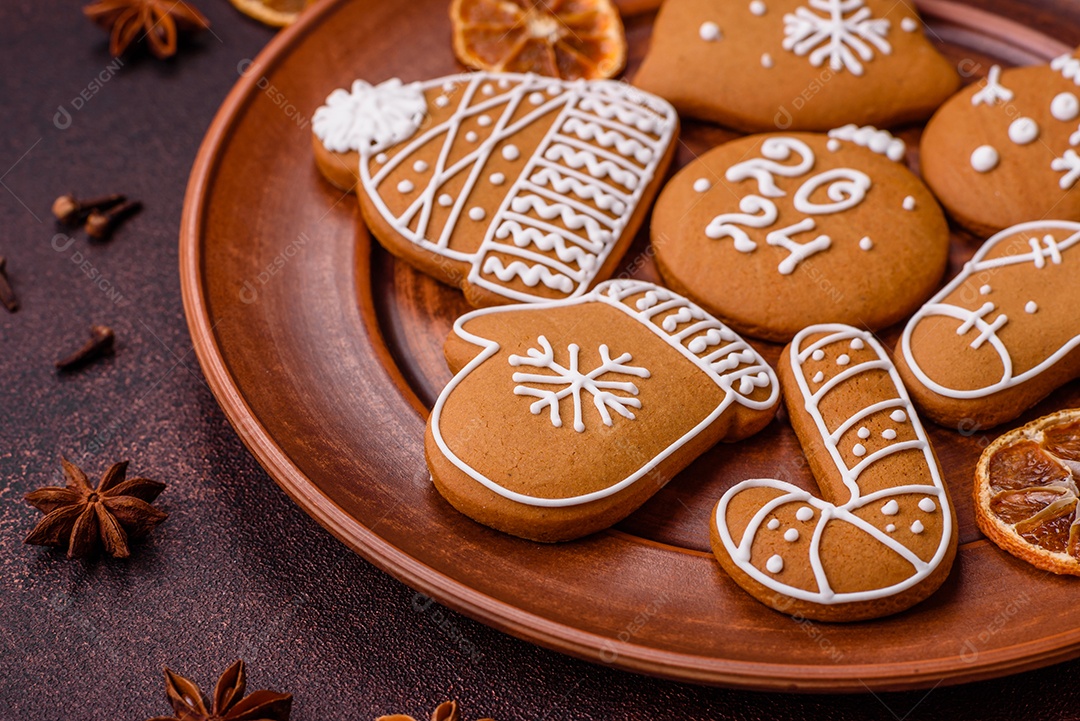 Lindos biscoitos de gengibre de Natal de cores diferentes em uma placa de cerâmica sobre uma mesa de concreto escuro