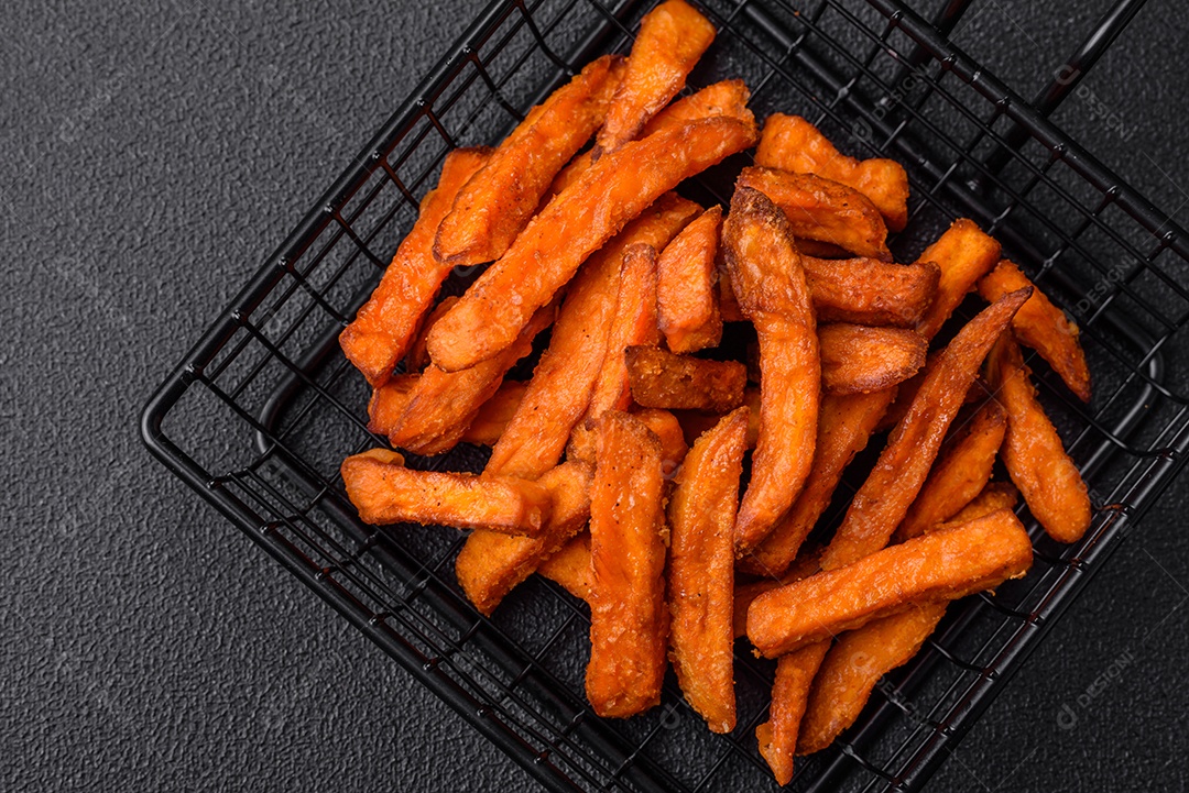 Deliciosas batatas fritas crocantes com sal, especiarias e ervas sobre um fundo escuro de concreto