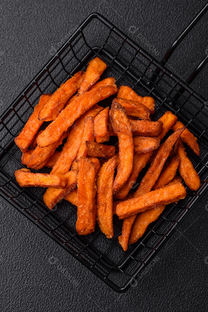Deliciosas batatas fritas crocantes com sal, especiarias e ervas sobre um fundo escuro de concreto