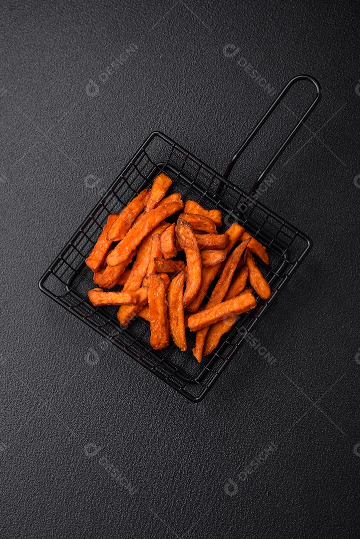 Deliciosas batatas fritas crocantes com sal, especiarias e ervas sobre um fundo escuro de concreto