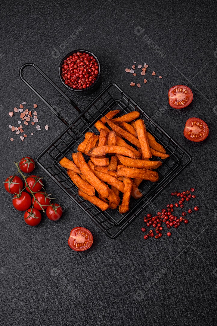 Deliciosas batatas fritas crocantes com sal, especiarias e ervas sobre um fundo escuro de concreto
