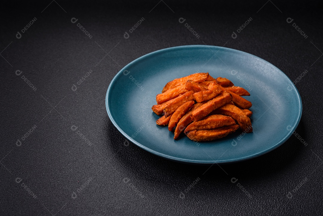 Deliciosas batatas fritas crocantes com sal, especiarias e ervas sobre um fundo escuro de concreto